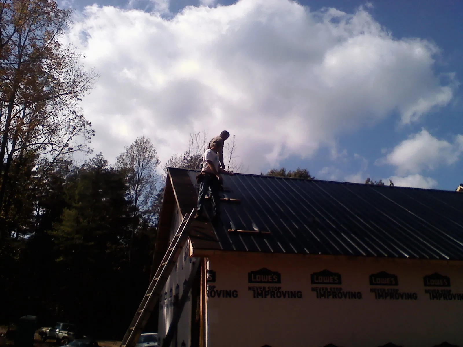 Roofer fastening dark metal panels high against a cloudy sky, from a Roof Inspection job in Brewster